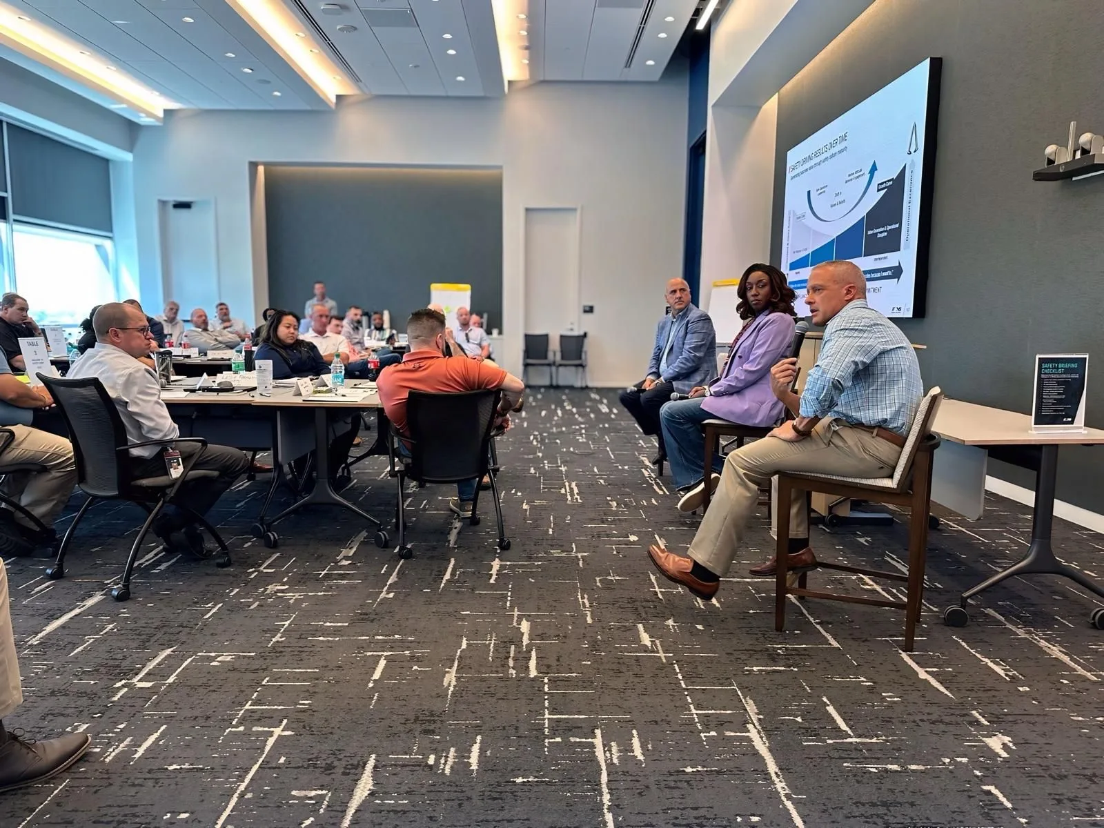 Rachel Bolton facilitating a seated leadership discussion with executives and a presentation screen visible behind them