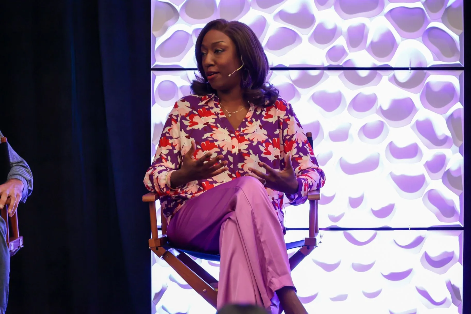 Rachel Bolton speaking on a panel in a floral blouse beneath a lit stage backdrop