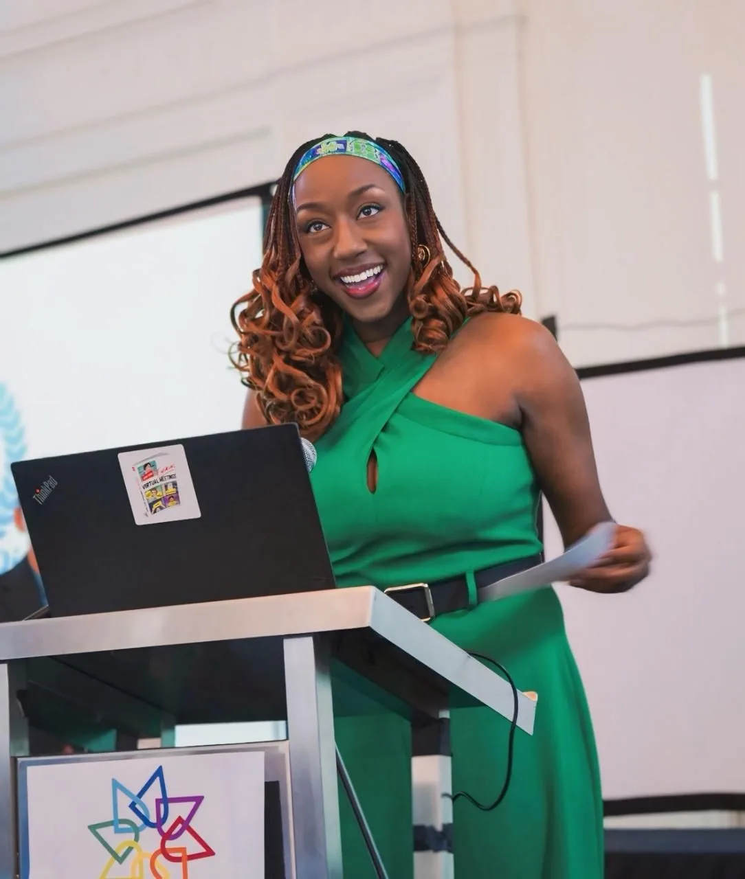Rachel Bolton smiling and addressing an audience from a podium in a bright green dress